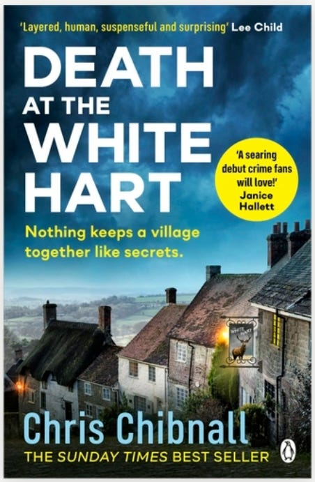 The book cover for Death at the White Hart by Chris Chibnall. The title is in large white letters against a dark blue, stormy-looking sky. Below the title is the tagline, "Nothing keeps a village together like secrets." The bottom half of the cover features a photograph of a quaint, old English village with thatched and slate roofs nestled in a misty valley. On the right, a pub sign depicting a stag—presumably The White Hart—hangs on one of the stone buildings. Above the title are a quote from Lee Child ("Layered, human, suspenseful and surprising") and a quote in a yellow circle from Janice Hallett ("A searing debut crime fans will love!"). The author's name, Chris Chibnall, is in large blue letters near the bottom, with "THE SUNDAY TIMES BEST SELLER" underneath.