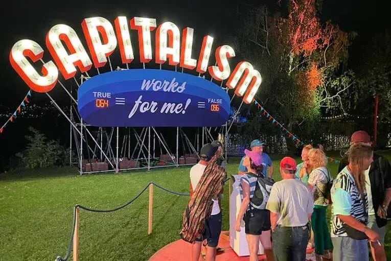 PHOTO Zürichur Theater Spektakel at night, participants looking up at lit up Capitalism sign at night