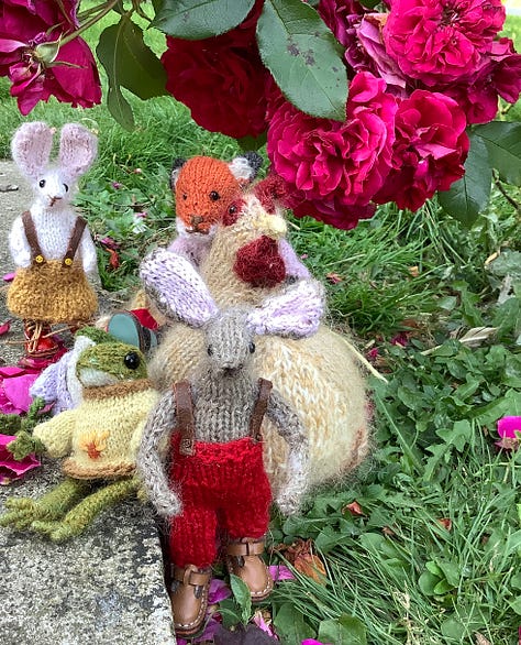 Knitted toys under a red rose bush surrounded by fallen petals