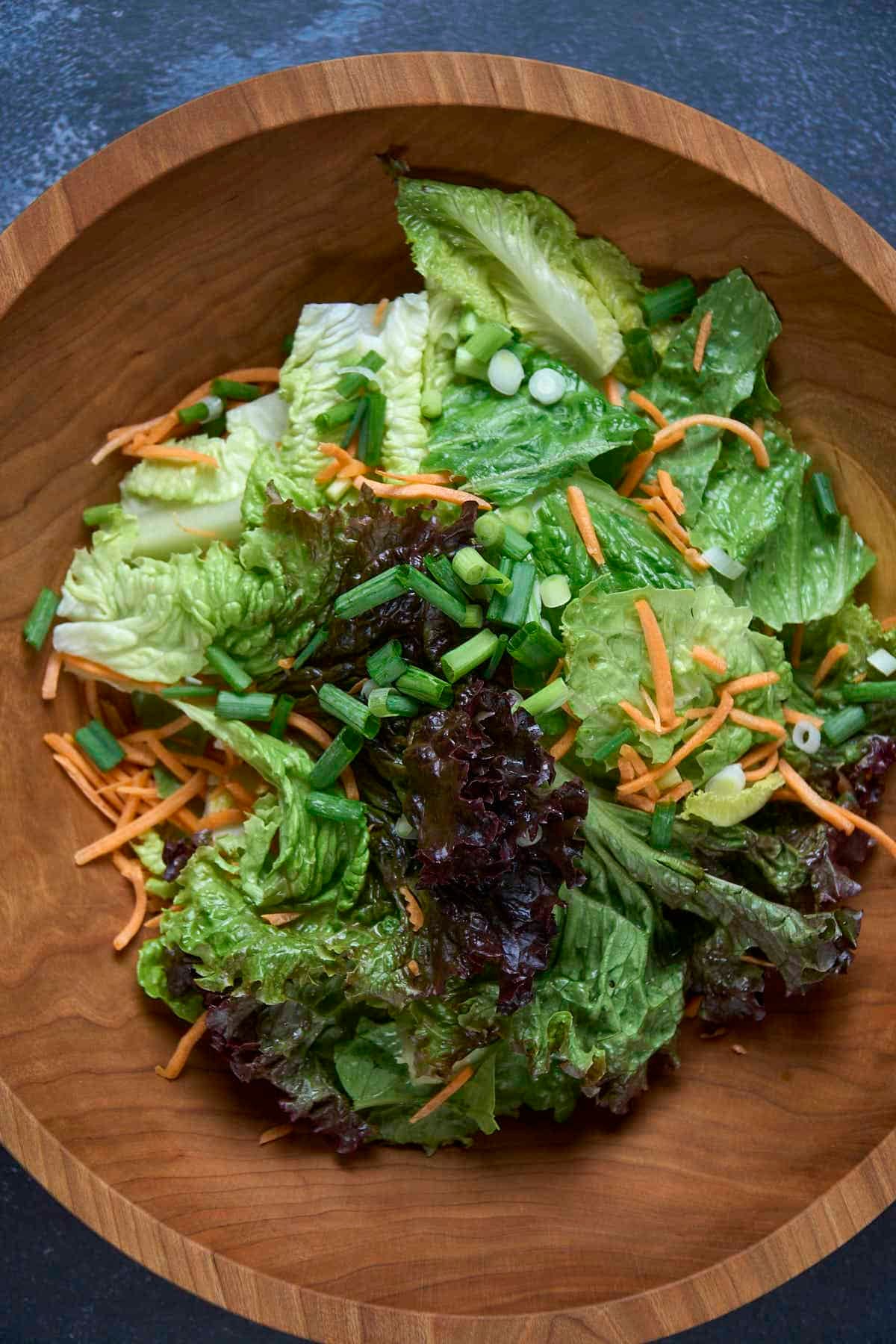 adding mixed greens into a salad bowl for korean lettuce salad