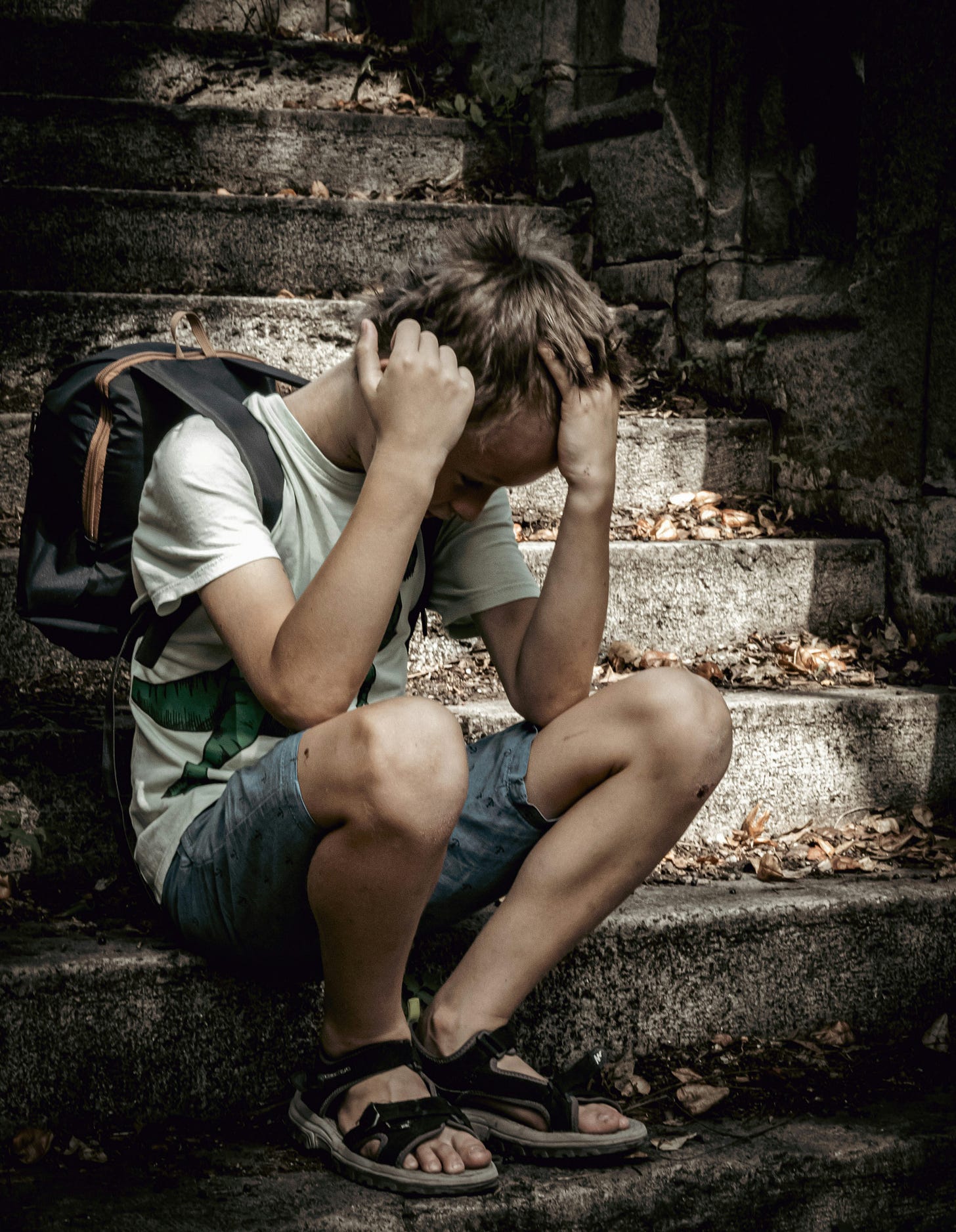 Picture of a boy sitting on stairs, head in hands.
