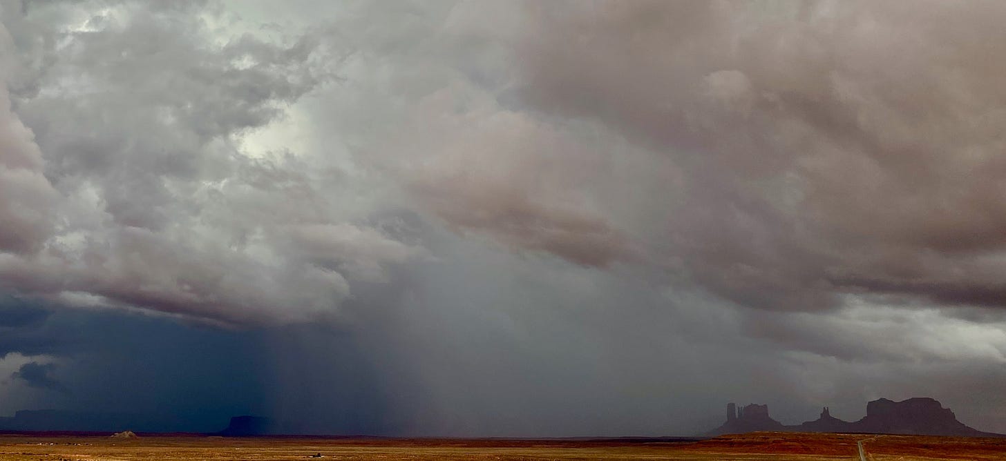 A wide shot of the spires of red rock in Monument Valley, Utah, almost completely obscured by a drenching thunderstorm.