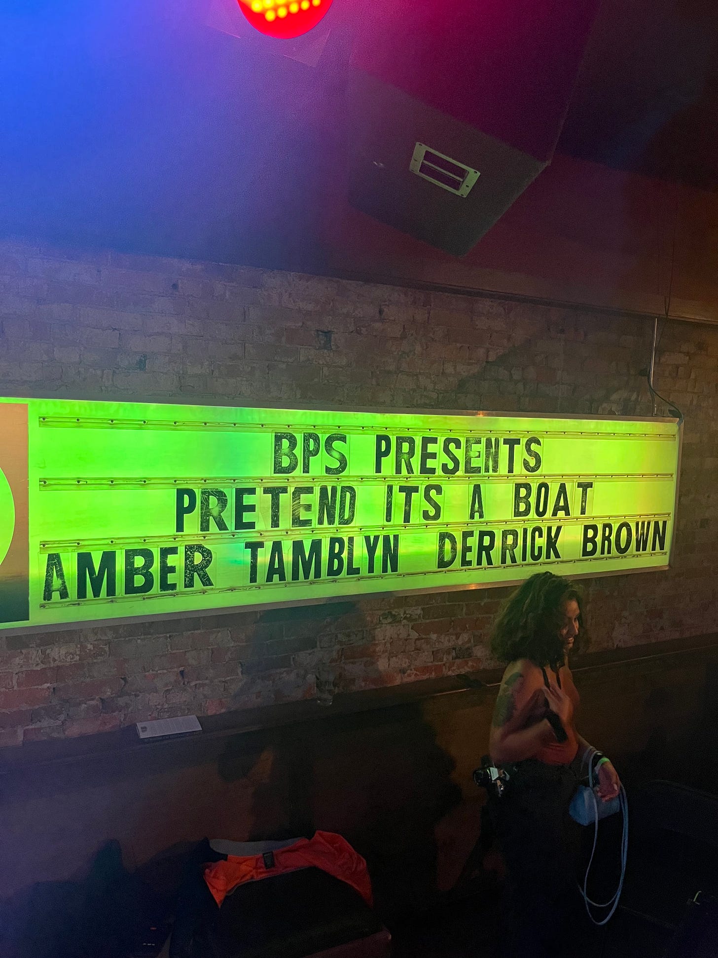 A marquee inside a venue against a brick wall. The marquee reads "BPS presents Pretend It's a Boat. Amber Tamblyn - Derrick Brown"