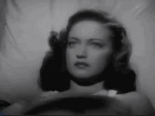 A woman hypnotizes another woman by swinging a pocket watch back and forth.