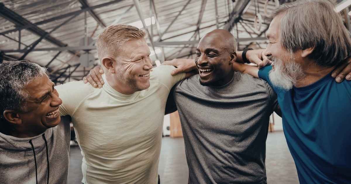 Four men with their arms around each other laughing