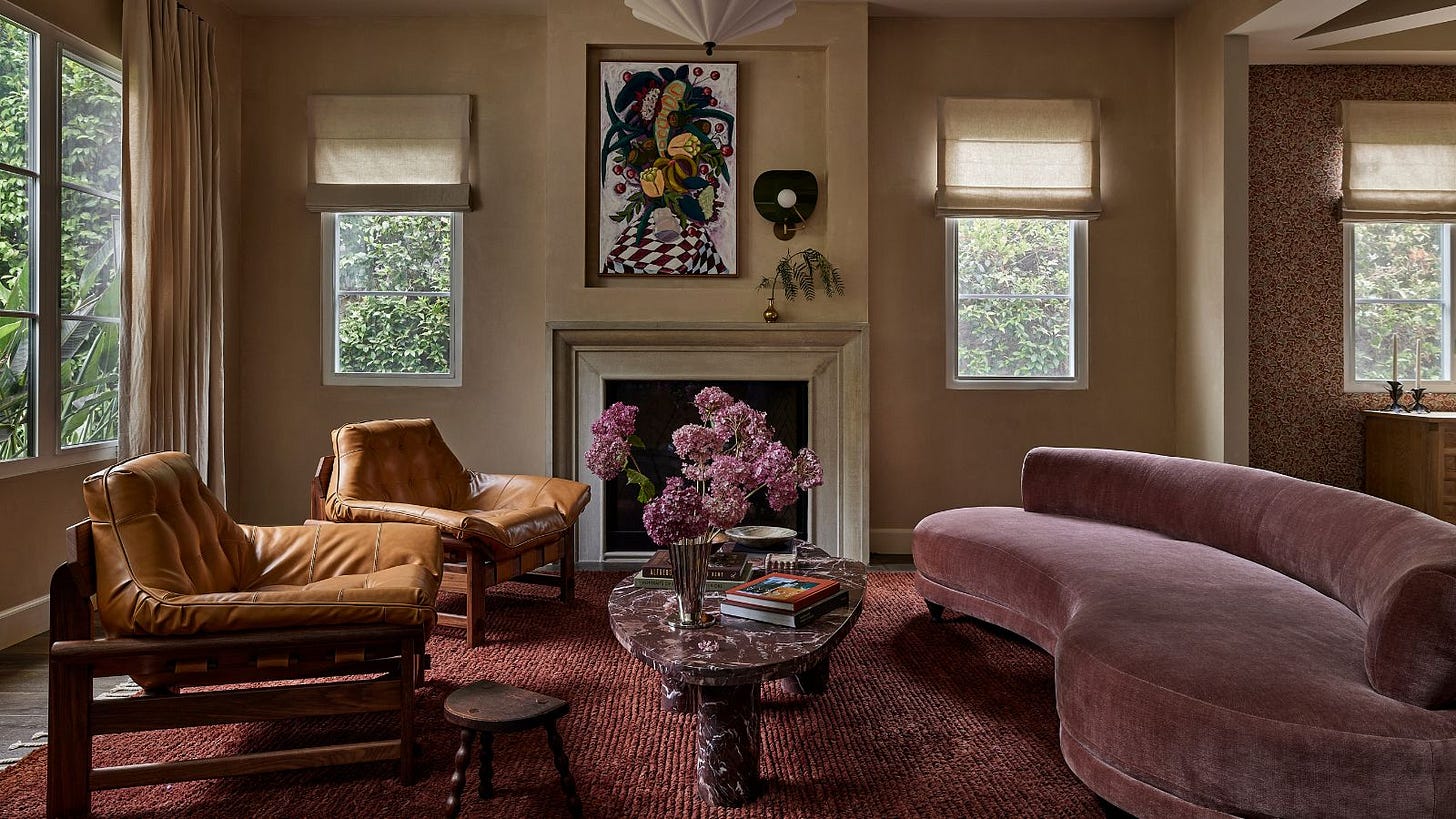 A modern living room with neutral walls, a fireplace, a plum-colored rug and a mauve curved sofa. 