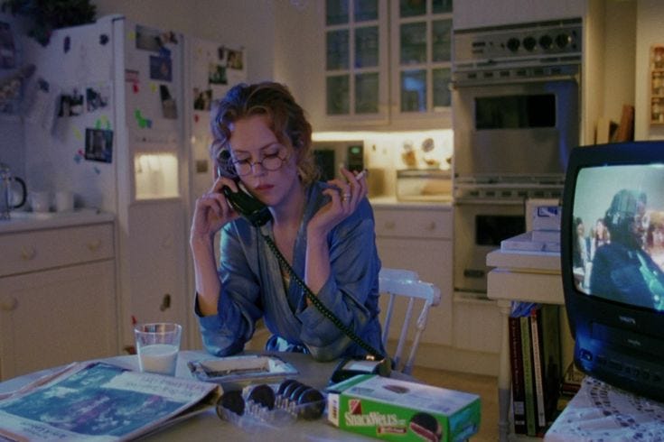 This may contain: a woman sitting at a kitchen table talking on the phone
