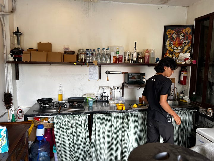 A man at a counter pressing a halved orange on a hand press, the juice running into a paper cup. An orange sliced in half, the skin green all the way around, the flesh ripe and orange inside. 