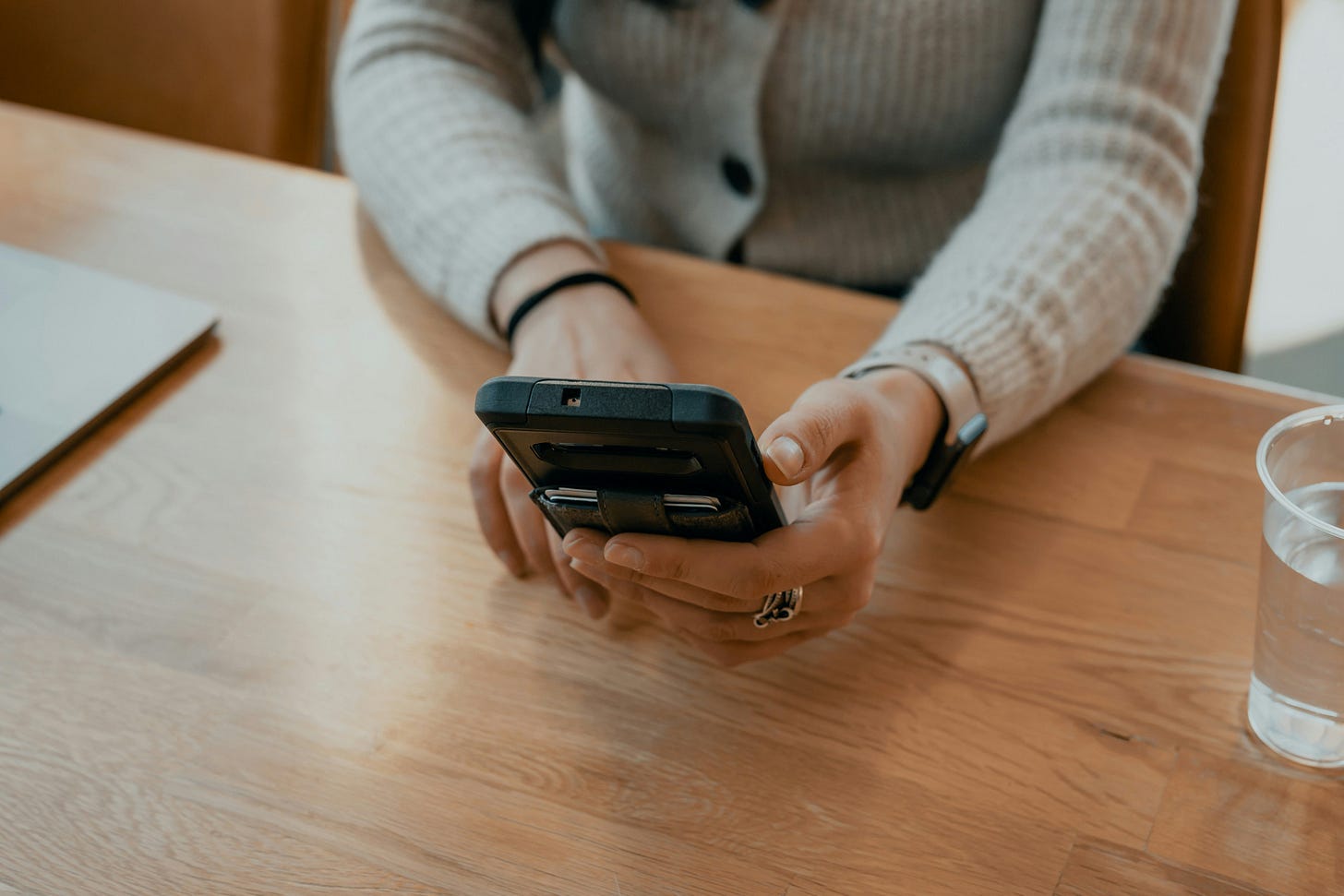 Woman's hands holding a black smart phone. The woman is wearing rings and a gray sweater
