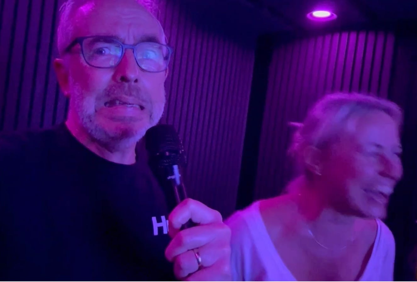 Andy and Julia laughing and singing during a karaoke performance at Center Parcs, illuminated by purple stage lighting. Andy holds a microphone and looks playfully unsure mid-song, while Julia laughs beside him. Andy and Julia laughing and singing during a karaoke performance at Center Parcs, illuminated by purple stage lighting. Andy holds a microphone and looks playfully unsure mid-song, while Julia laughs beside him.