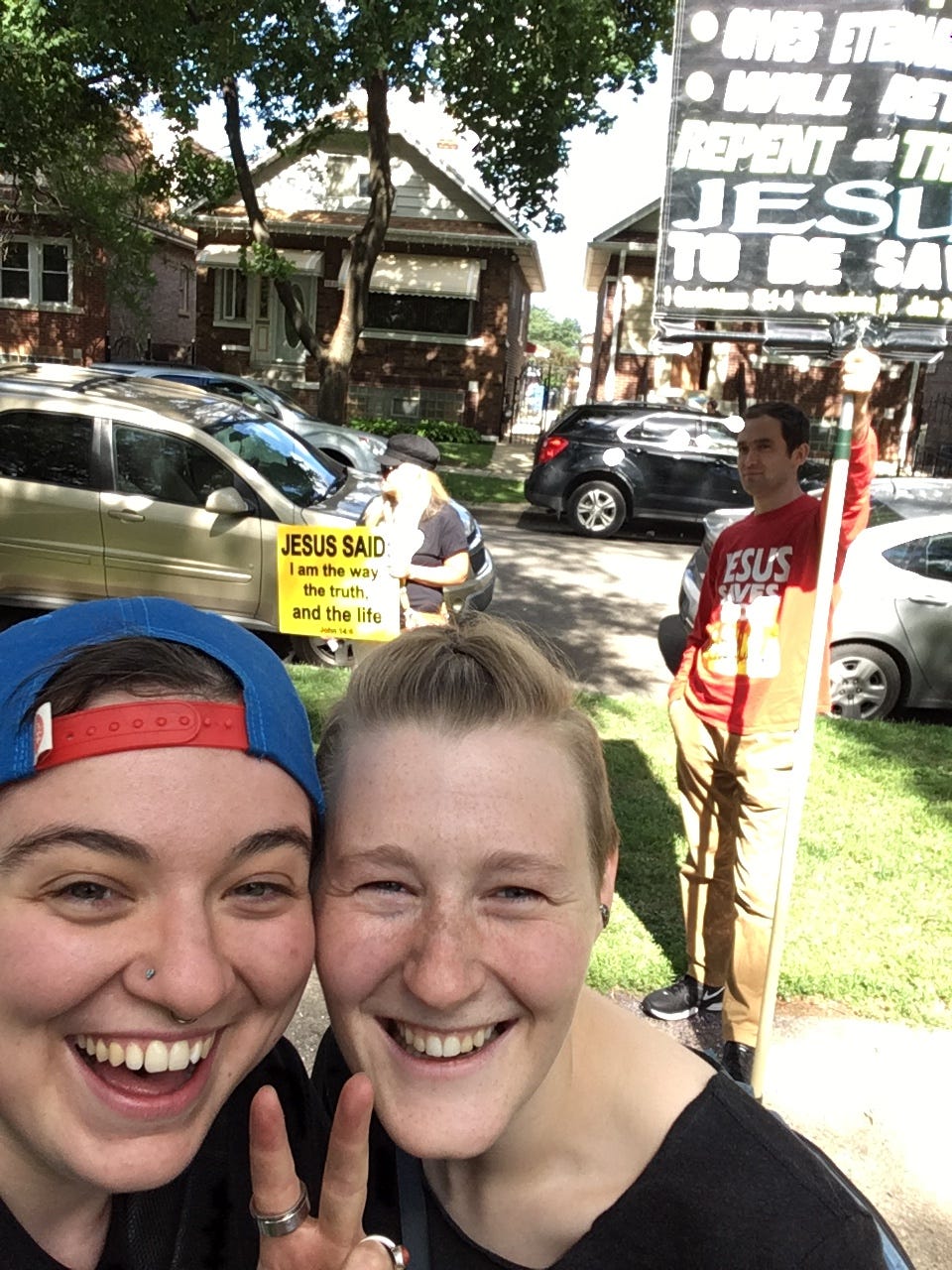 Me and my friend Qwill in front of evangelical protestors at the 2017 Dyke March; we're smiling big and they are not