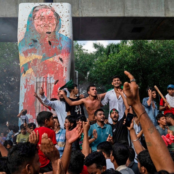 Protesters celebrate beside a defaced portrait of Sheikh Hasina after news of her resignation, in Dhaka on Monday
