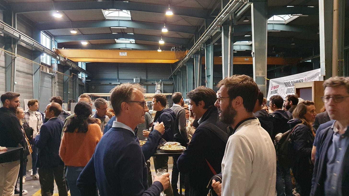 Photo des participants à l'événement Post levée de fonds. On y voit les participants debouts réunis autour de tables rondes lors de l'apéritif dînatoire proposé dans le hangar de la S-Factory.