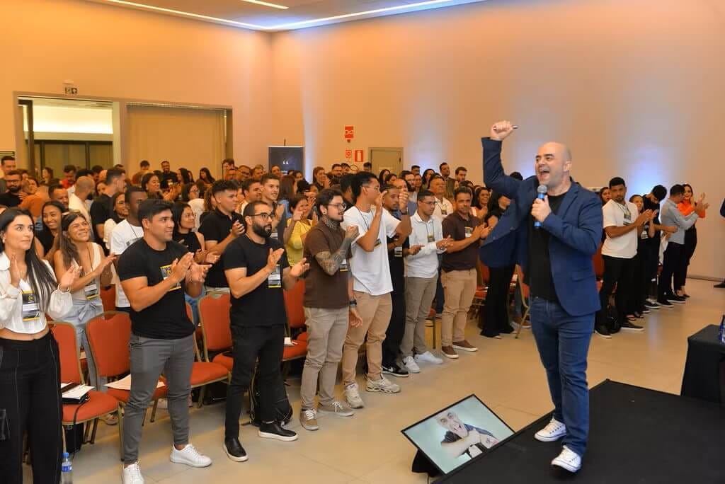 imagem de um palestrante com uma das mãos para cima comemorando enquanto um auditório com mais de 300 pessoas aplaude de pé