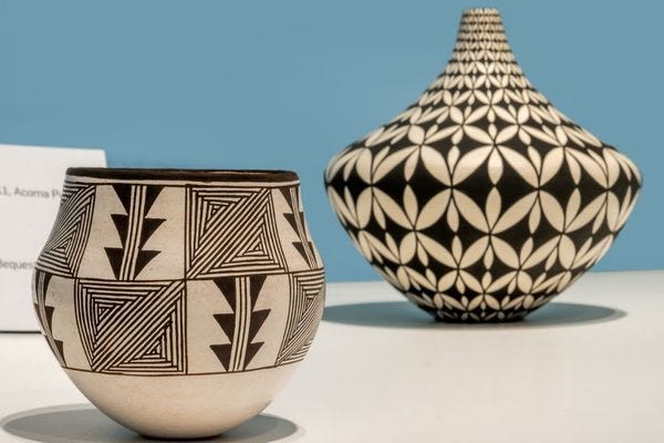 Two Pueblo ceramic vessels with black-and-white geometric designs. The piece in the foreground is round with triangular patterns and the piece in the background is a pointed vase with interlocking floral motifs.