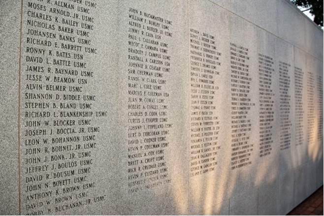 Close-up view of engraved names of fallen U.S. Marines, sailors, and soldiers on the Beirut Memorial wall in Jacksonville, North Carolina, illuminated by afternoon light.