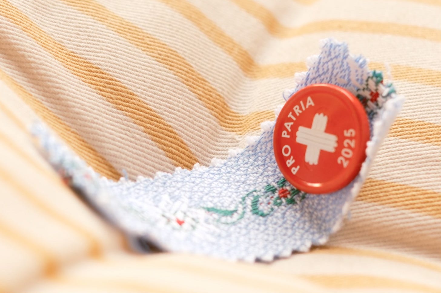 A Swiss 20-franc banknote with a red circular 'Pro Patria 2025' commemorative pin or button placed on top, lying on a light wooden surface.