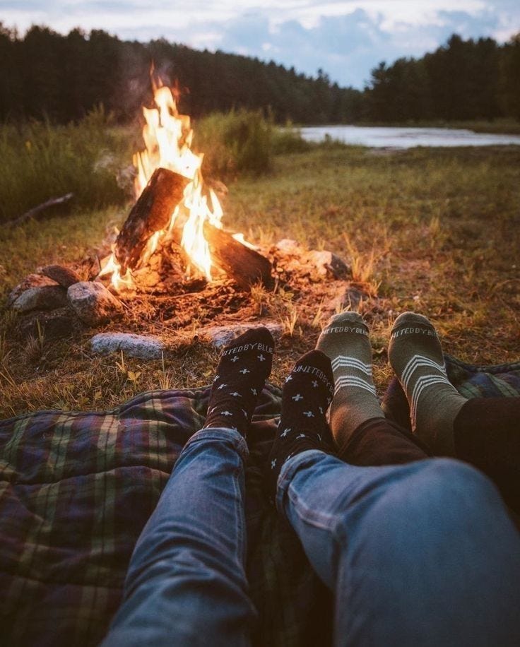 a campfire with two people sitting on a blanket near it but you can only see their feet