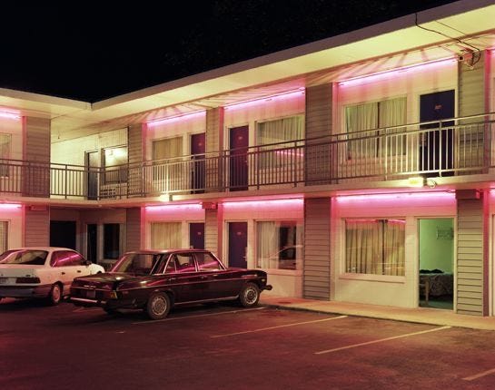 This may contain: two cars parked in front of an apartment building with pink lights on the windows and balconies