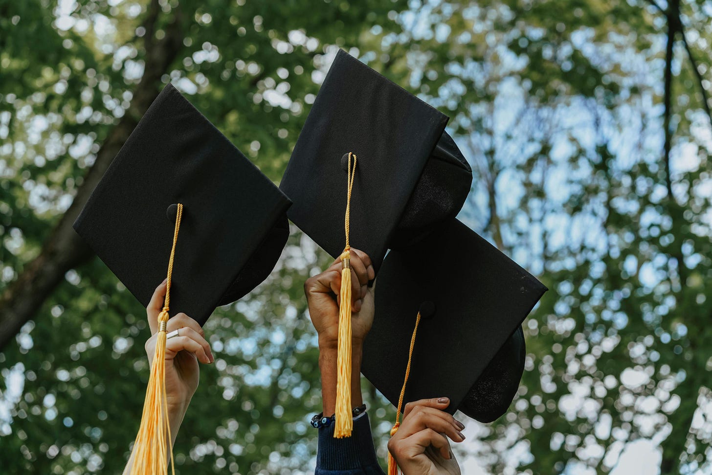 Students holding up university graduation hats Students holding up university graduation hats