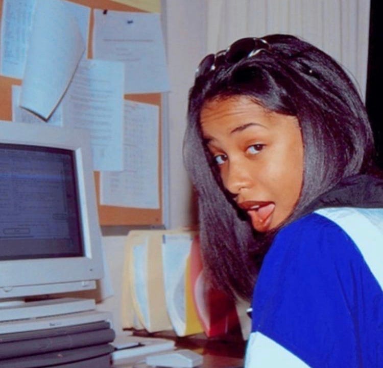A woman beside a beige CRT monitor and a wall of workplace papers.