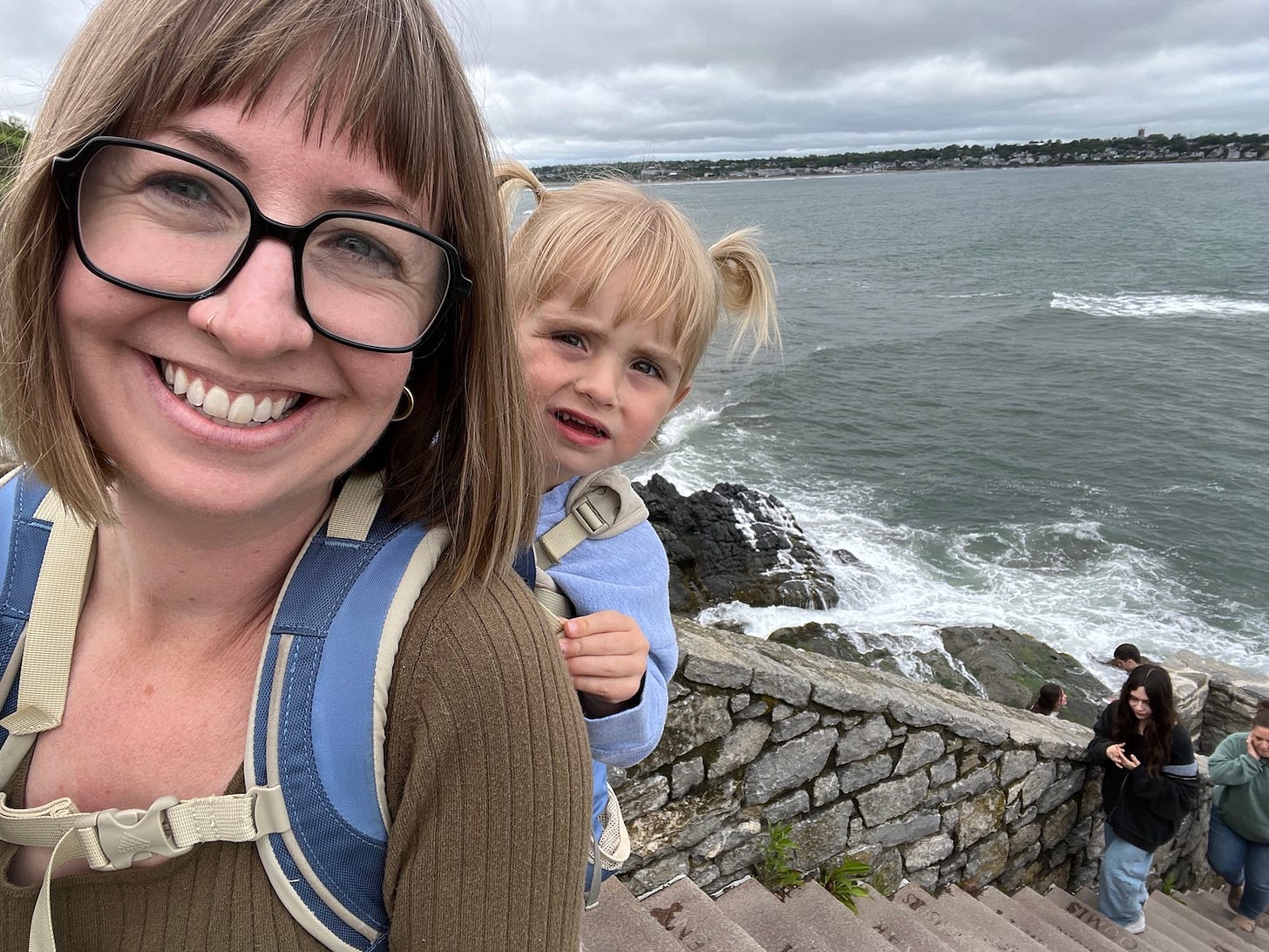 Woman with toddler on back are climbing steep stairs by the ocean