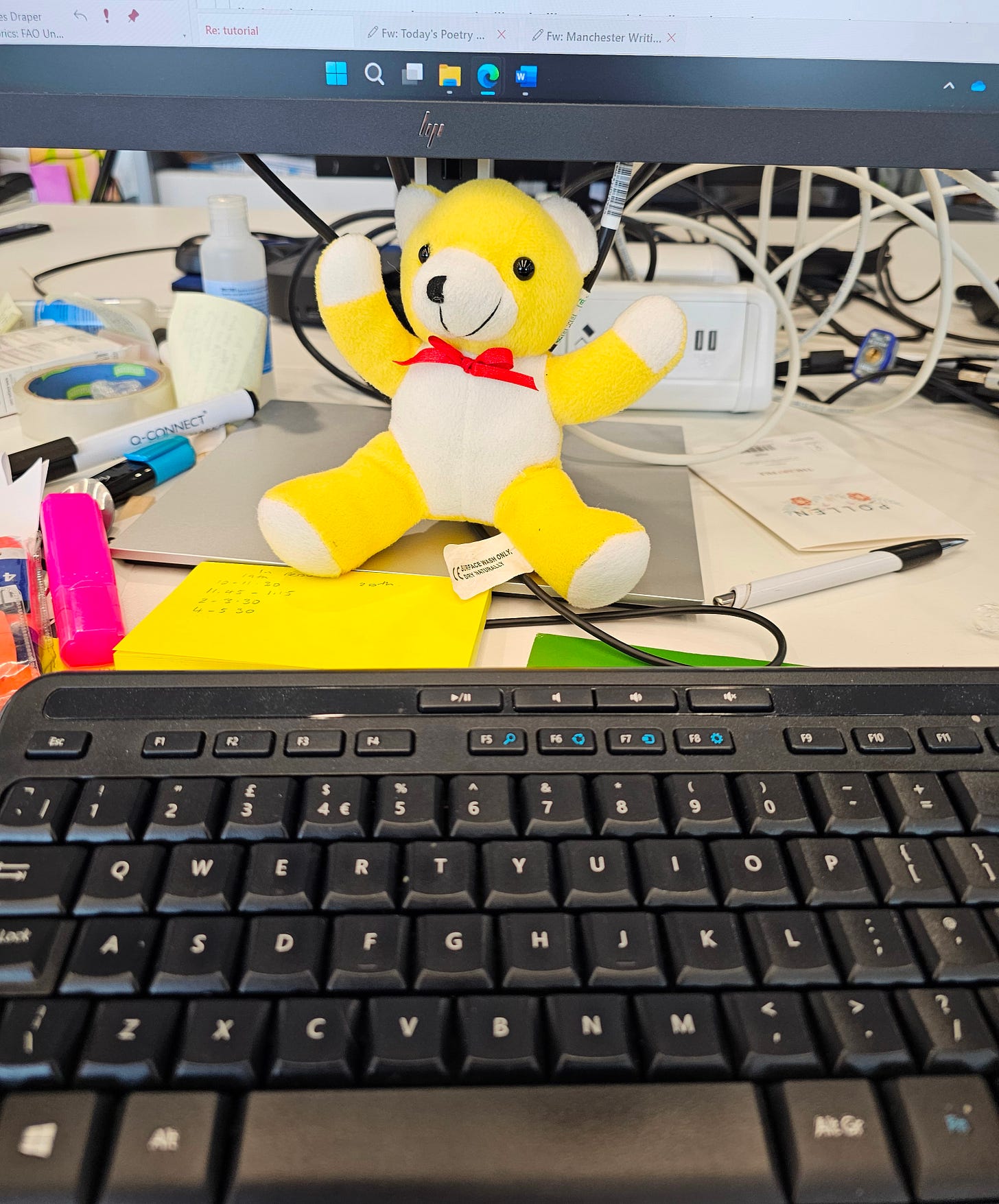 Picture of my computer keyboard at work with one of my daughter's teddies propped up in front of the screen.  Yellow Bear comes to work with me if I'm going to be back late and miss a bedtime.