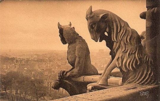 This may contain: two statues sitting on top of a building next to a cityscape with buildings in the background