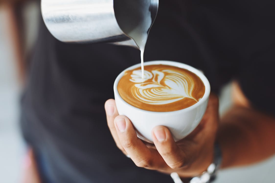 Free Close-up of a barista pouring milk to create latte art in a coffee cup. Stock Photo