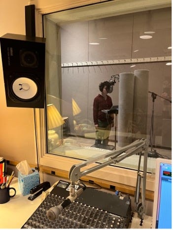 Left image description: Rachel, a femme with curly dark hair and olive skin, stands at a microphone in a studio, reading from a laptop. Right image description: View over an audio control panel and engineer’s microphone into a recording studio where Rachel stands at a microphone.