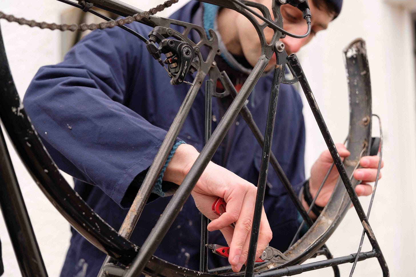 A person stands by an old bike with its wheel missing. They lean over the bike inspecting the damage and attempt a repair. 