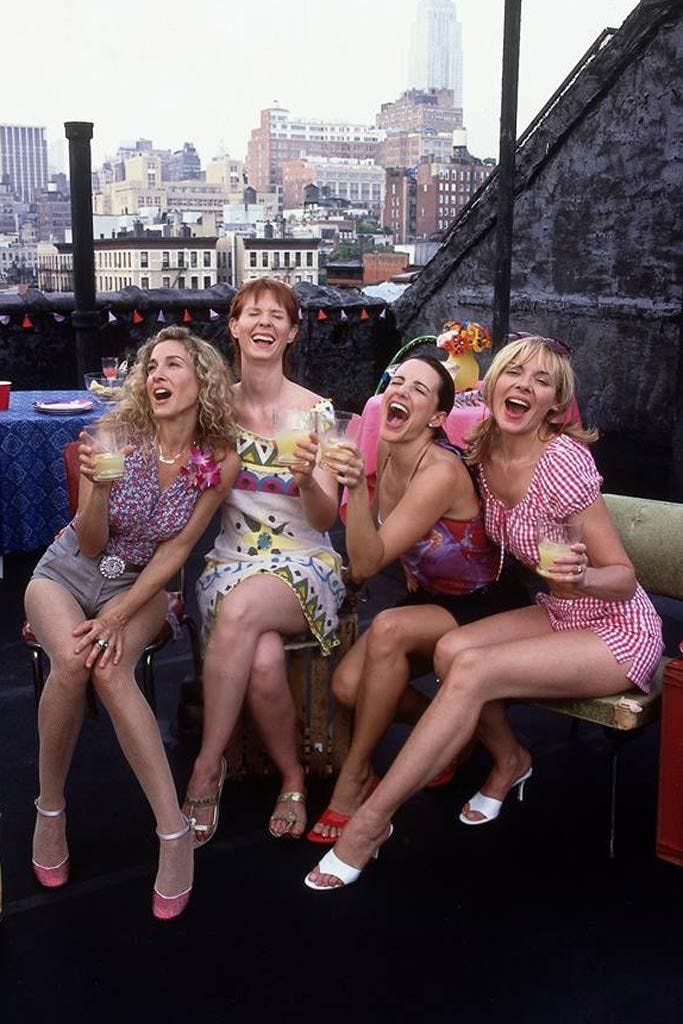 This may contain: four women in bathing suits are sitting on a bench and drinking drinks from wine glasses