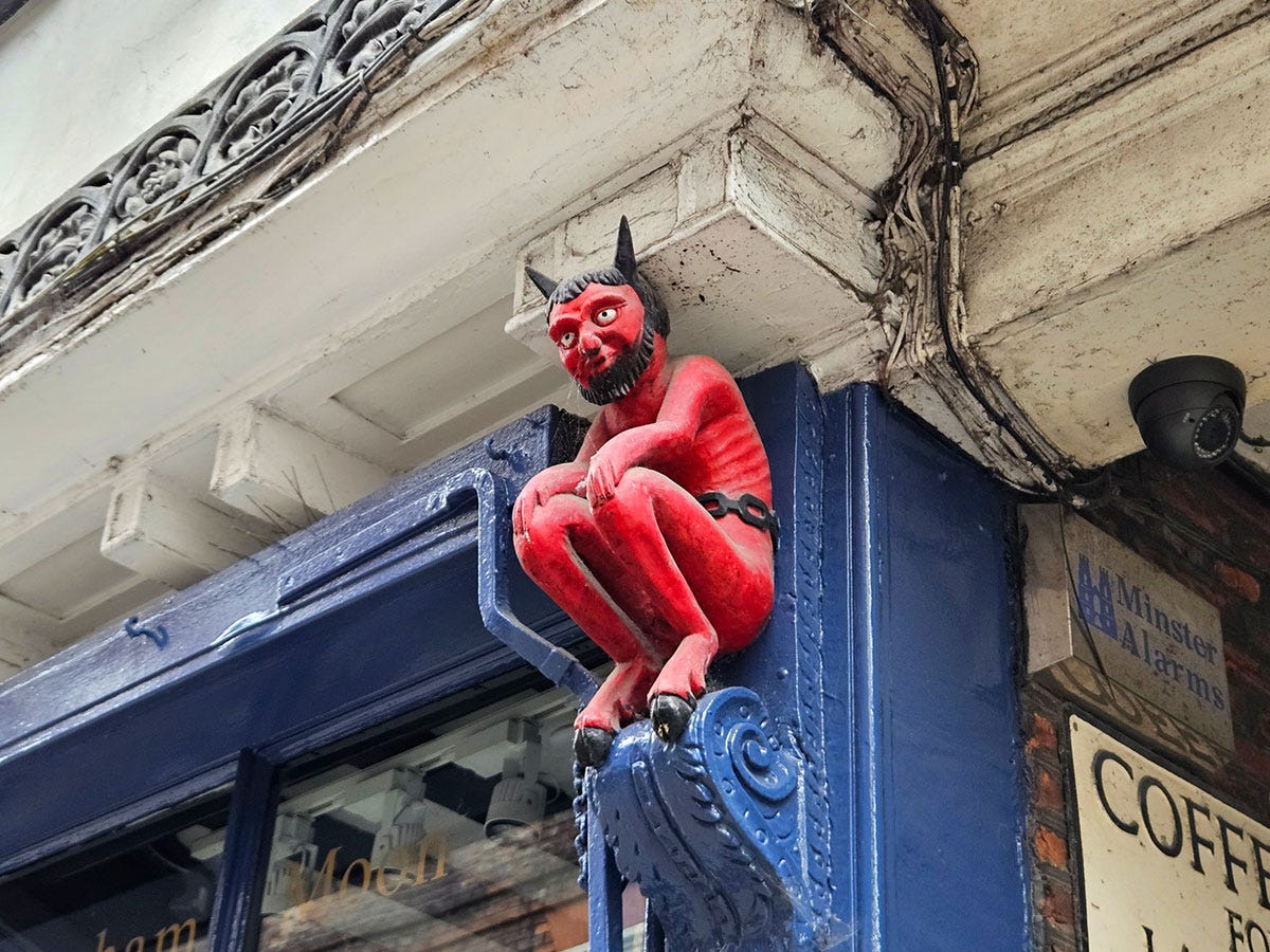 A red wooden devil figure perched on a column on the facade of a shop
