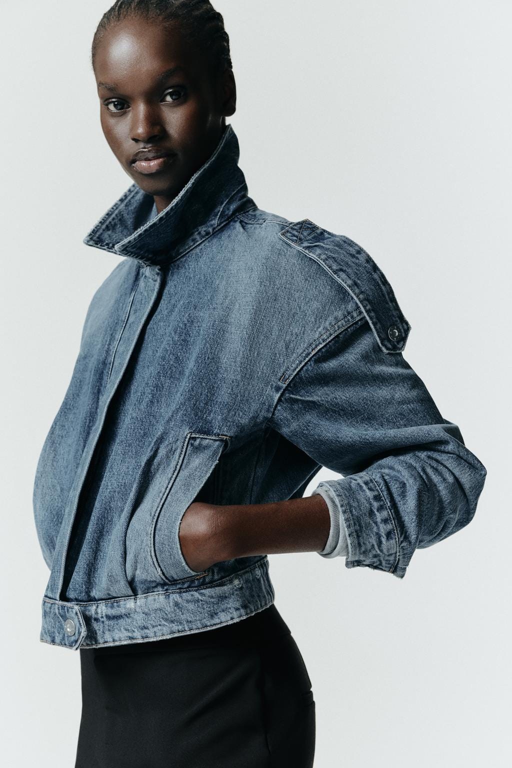 Close-up of a short blue denim jacket with a shirt collar, long sleeves, front pockets, and a zip fastening.