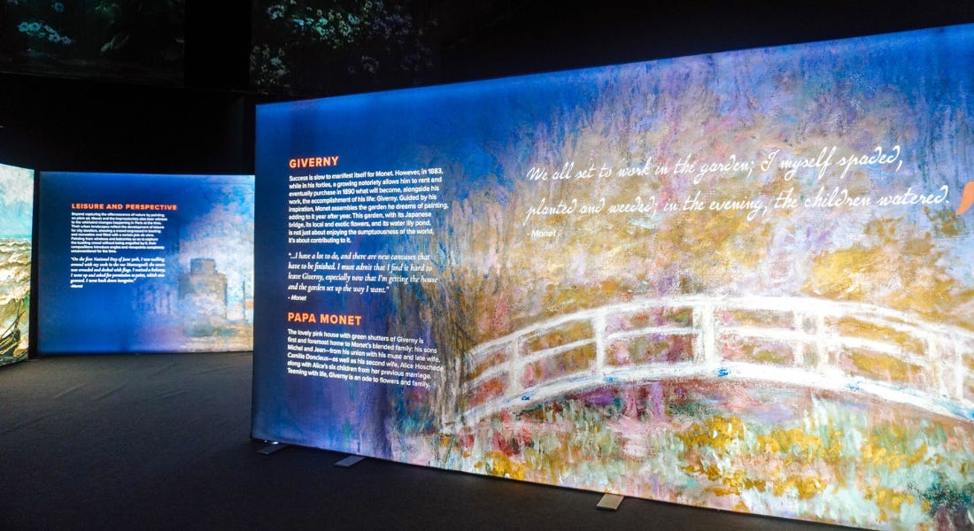 A dark room with large information panels with white text, navy blue, and paintings A dark room with large information panels with white text, navy blue, and paintings