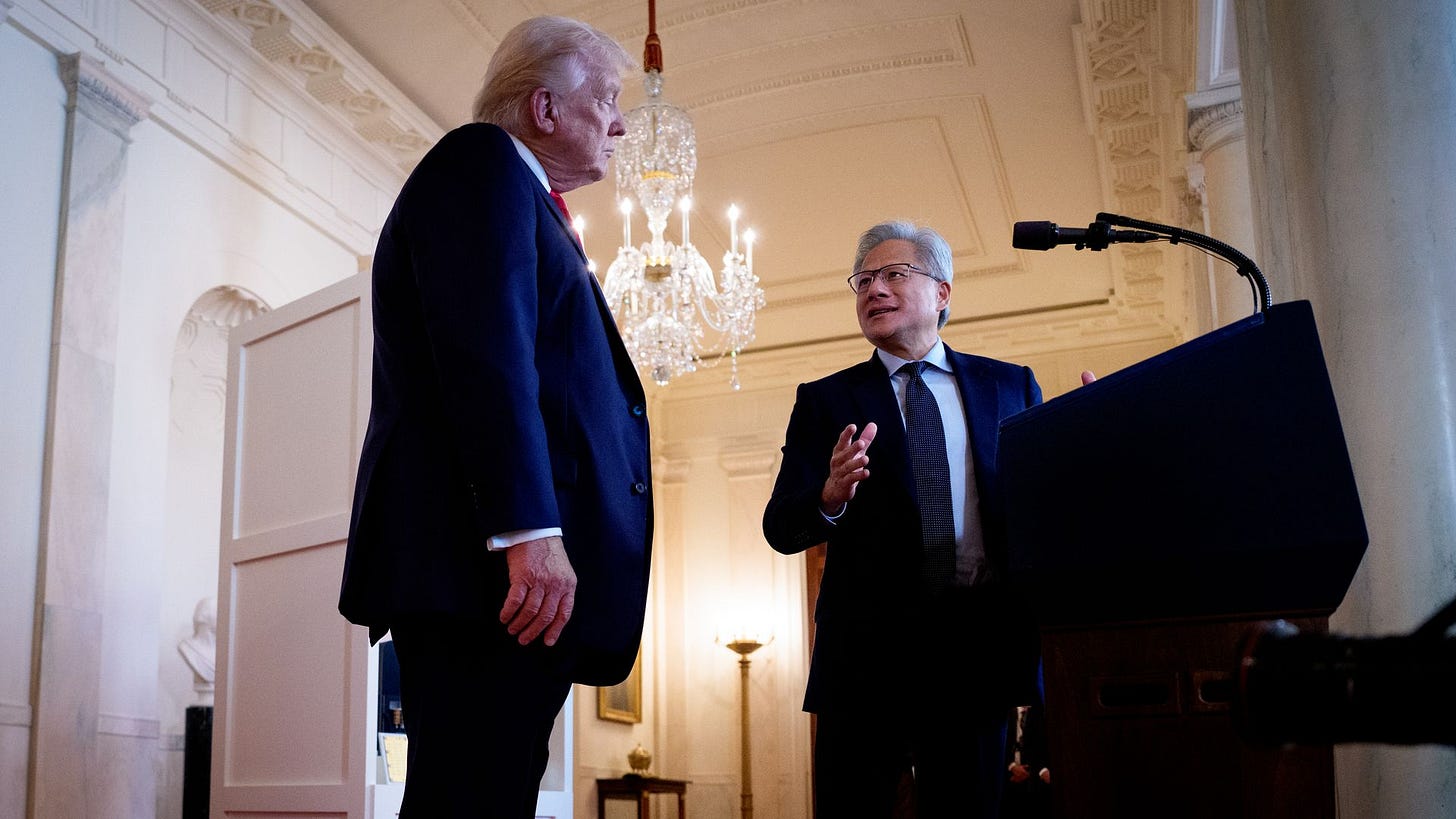 Two people in dark suits engage in conversation in an ornate room with a chandelier, red carpet, and podium with microphone, lit by warm wall sconces and a floor lamp.