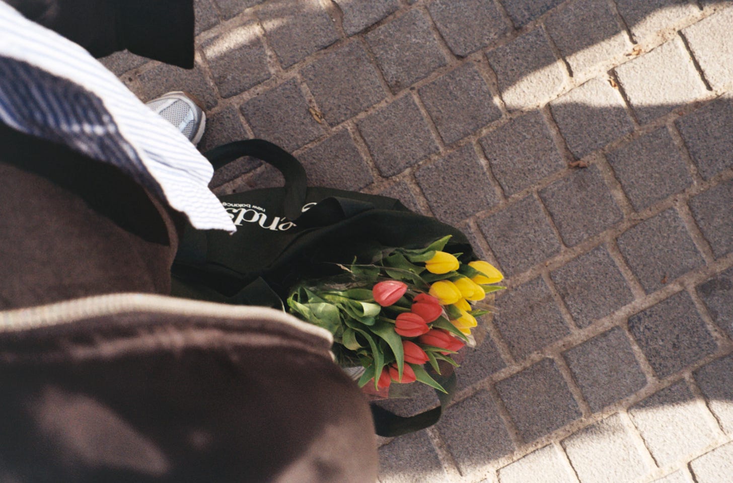 A film photo from above—my dark green tote bag at my feet, two bouquets of tulips (pink and yellow) bringing a pop of colour.