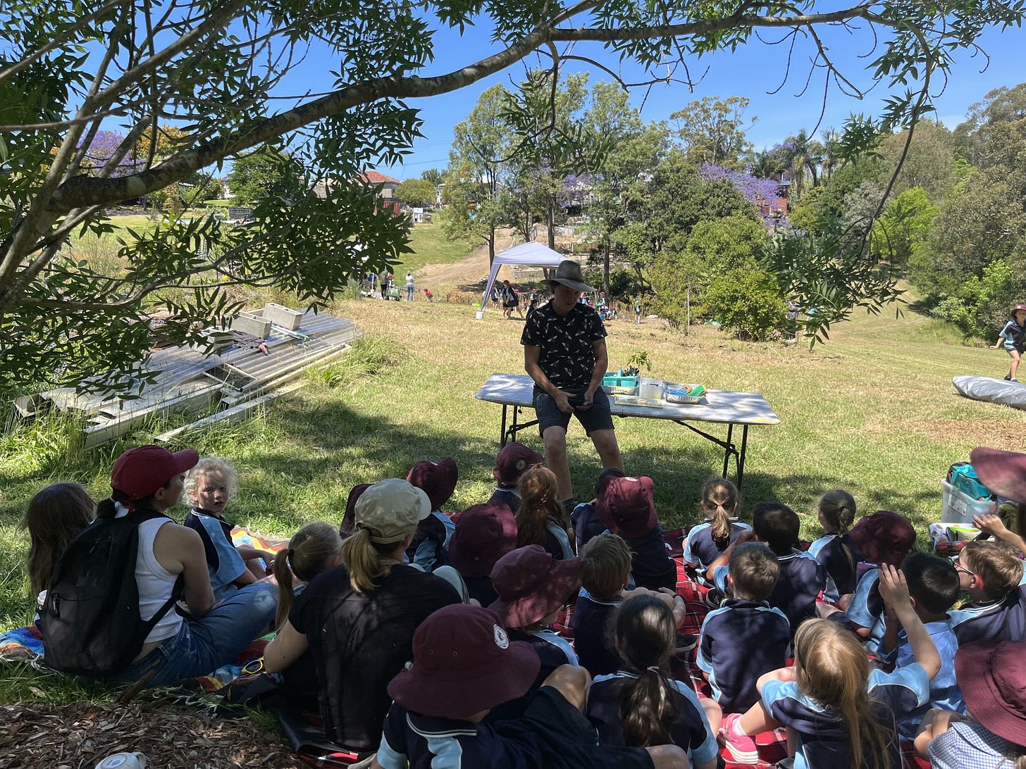 School kids sitting under a tree listening to a talk about tiny forests