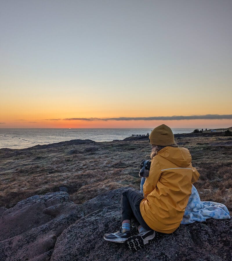 Haley, a woman in a yellow coat, and Scout, a blue heeler wrapped in a blanket, watch the first sunrise in North America at Cape Spear in Newfoundland Haley, a woman in a yellow coat, and Scout, a blue heeler wrapped in a blanket, watch the first sunrise in North America at Cape Spear in Newfoundland