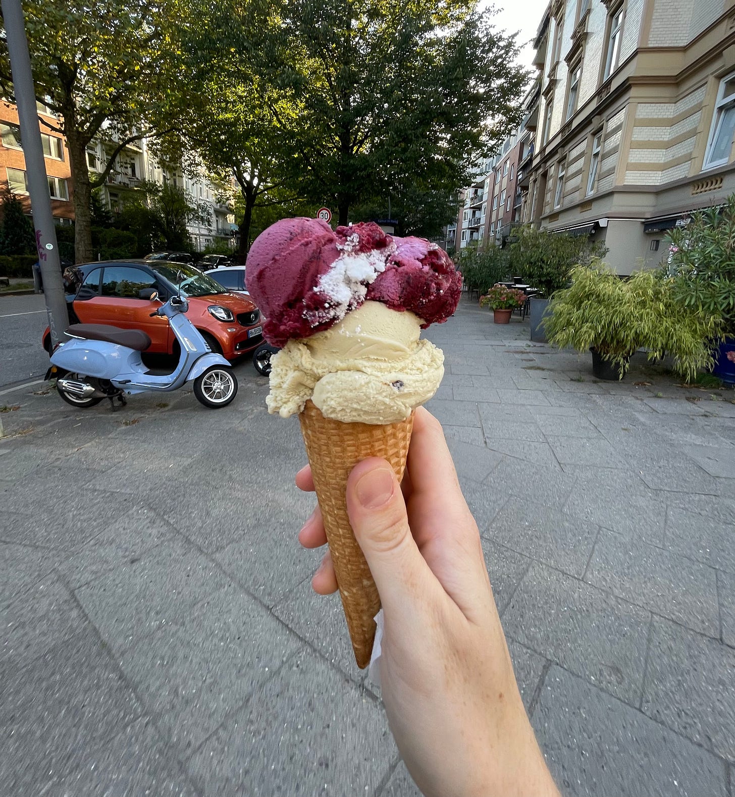 Maeve's hand holding up an ice cream cone with two scoops of ice cream on a warm summer day.