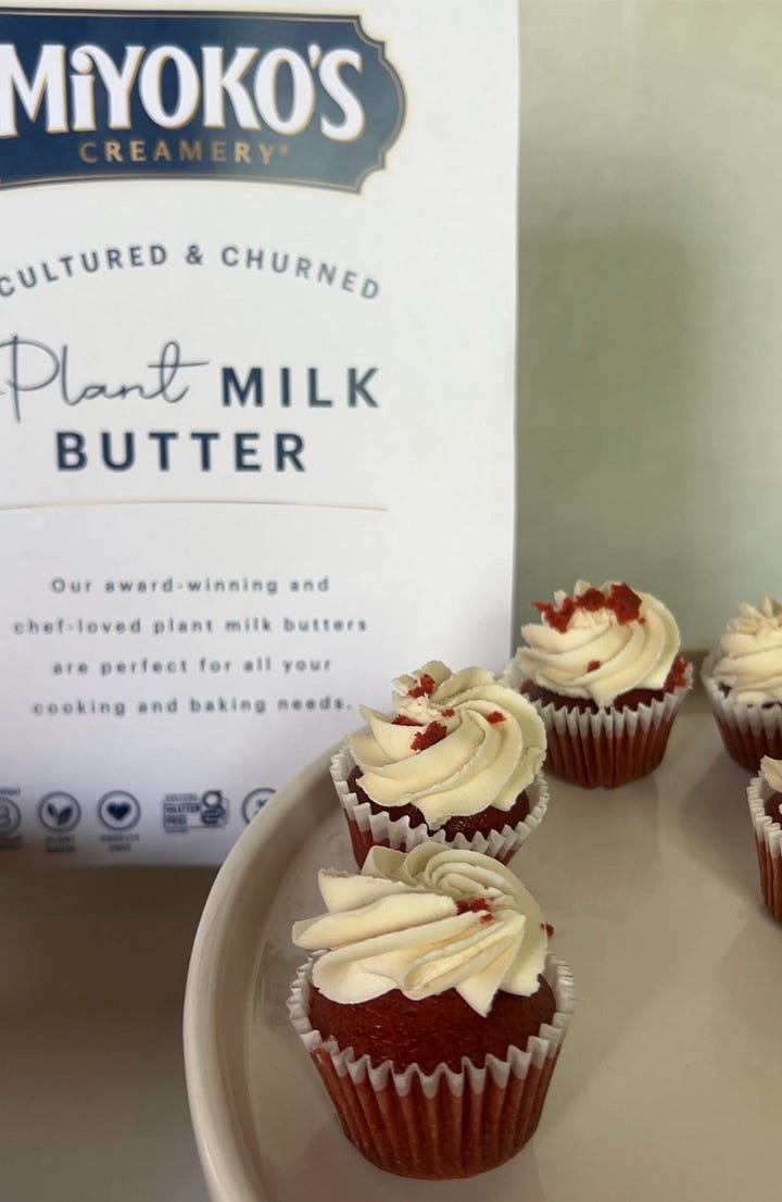 A plate of red velvet cupcakes and a woman holding a piece of vegan fried chicken
