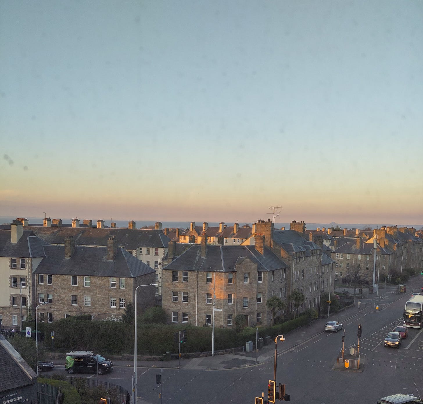 A picture of a street at sunset, your can see the ocean just over the rooftops.