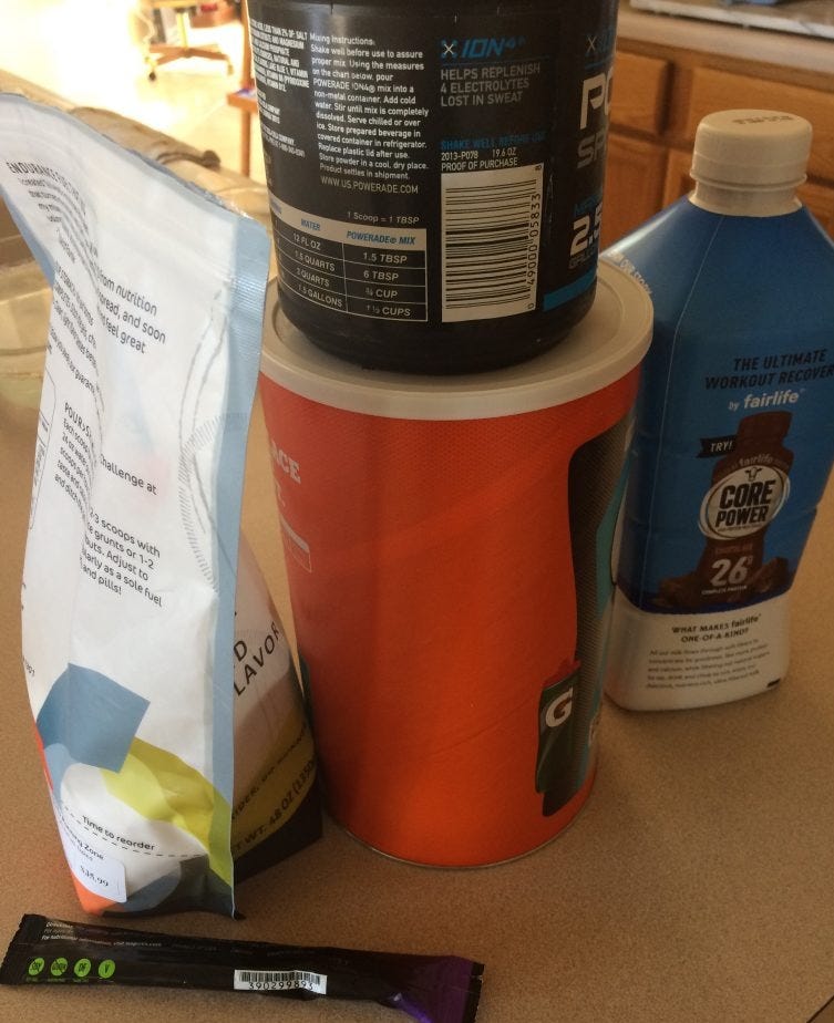 An assortment of training recovery nutrition and hydration products are depicted, including an orange canister, Fairlife Milk bottle, nad a powdered nutrition white bag An assortment of training recovery nutrition and hydration products are depicted, including an orange canister, Fairlife Milk bottle, nad a powdered nutrition white bag