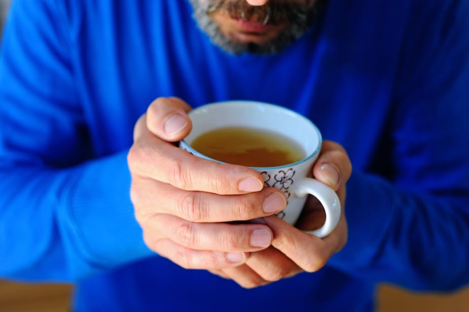 A middle-aged man holds a cup of green team in his hands. A middle-aged man holds a cup of green team in his hands.