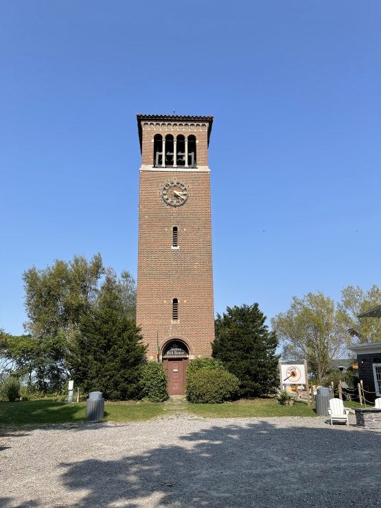 The Miller Bell Tower stands tall against a brilliant blue sky at Chautauqua Institution. This iconic brick structure, with its Romanesque arches and clock face, has been a lakeside landmark since its construction in 1911. ©Tamara MC, Ph.D.