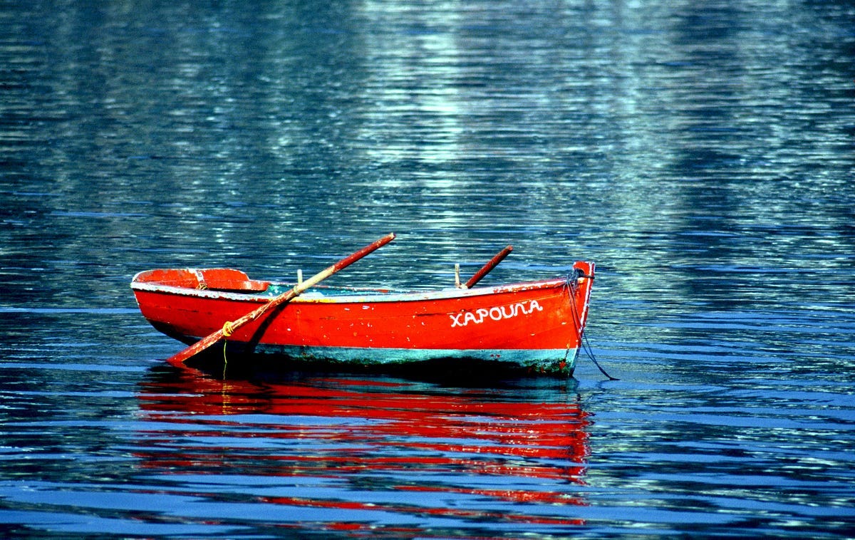 A bright red one man skiff on blue water A bright red one man skiff on blue water