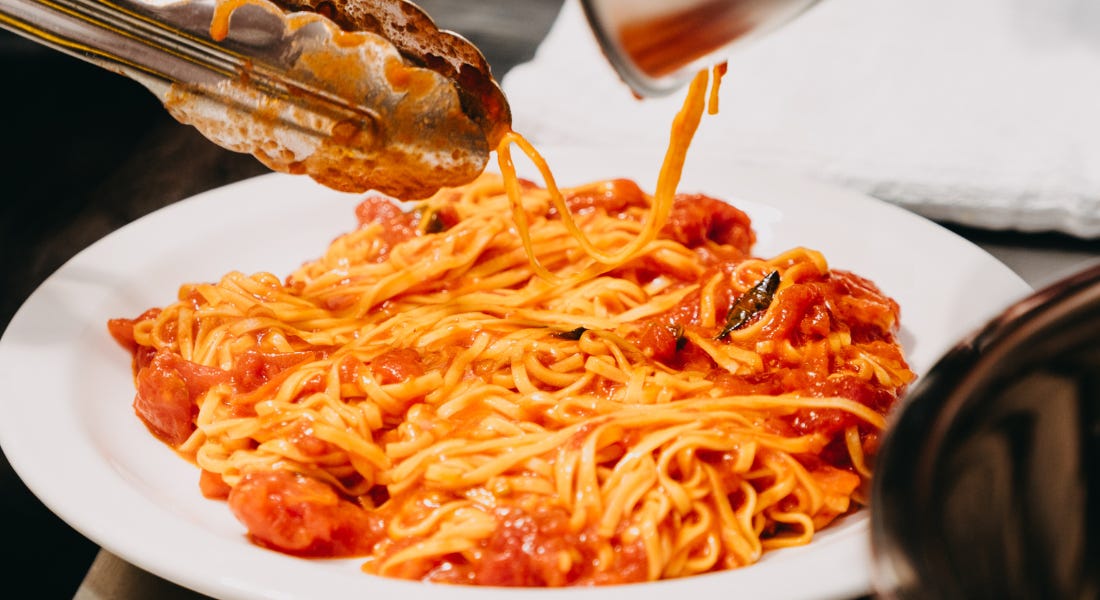 A plate of pasta with red sauce on a white plate with tongs above it A plate of pasta with red sauce on a white plate with tongs above it