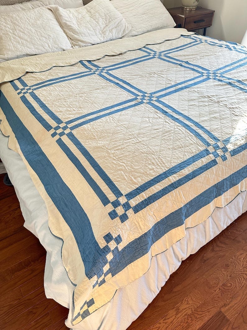 May include: A white and blue quilt with a scalloped edge. The quilt is made with a white fabric and has blue stripes and squares. May include: A white and blue quilt with a scalloped edge. The quilt is made with a white fabric and has blue stripes and squares.