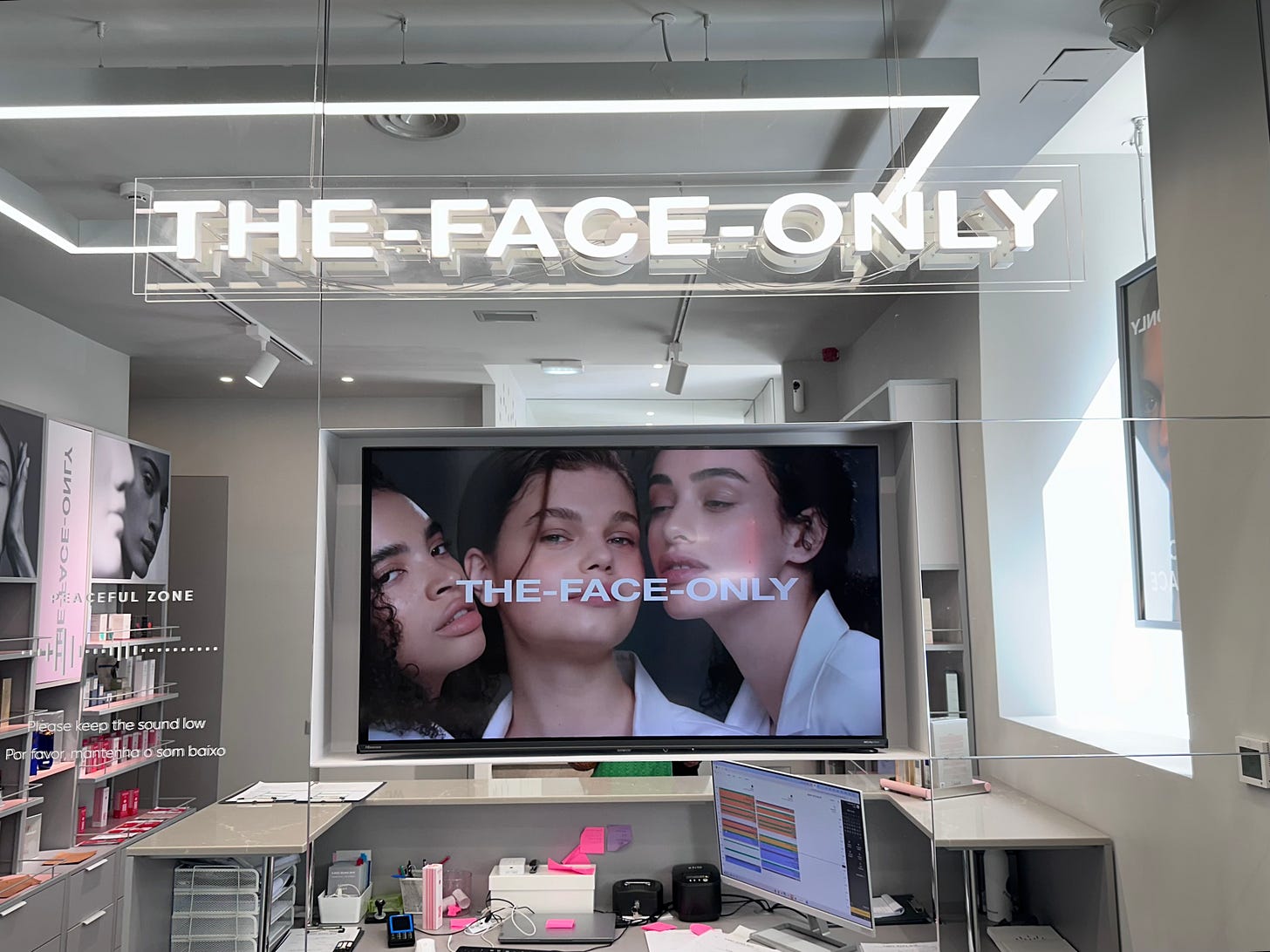 Reception area at The Face Only in Lisbon, with the illuminated store sign above a screen showing three models Reception area at The Face Only in Lisbon, with the illuminated store sign above a screen showing three models