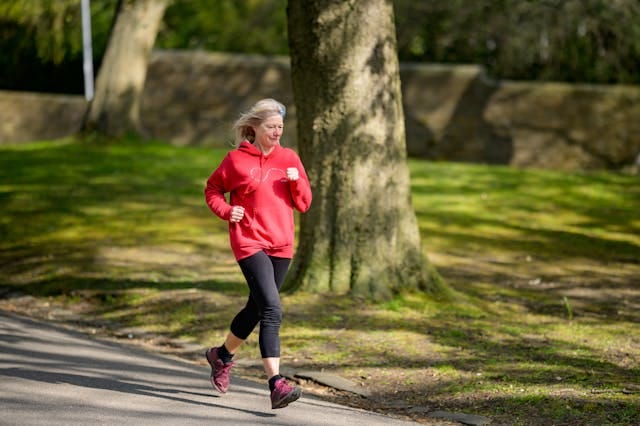 Older woman in red hoodie and leggings jogging in a park